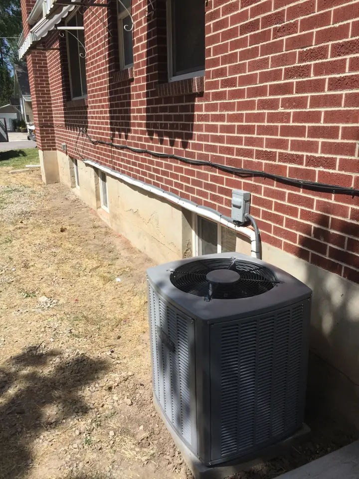Newly installed central air conditioner condenser on a pad beside a red brick home, a job by I Know A Guy HVAC in the Salt Lake Valley