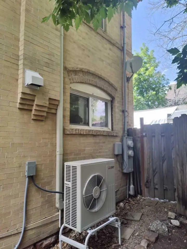 Newly installed Mitsubishi ductless mini-split outdoor unit beside a brick home, a job by I Know A Guy HVAC in the Salt Lake Valley